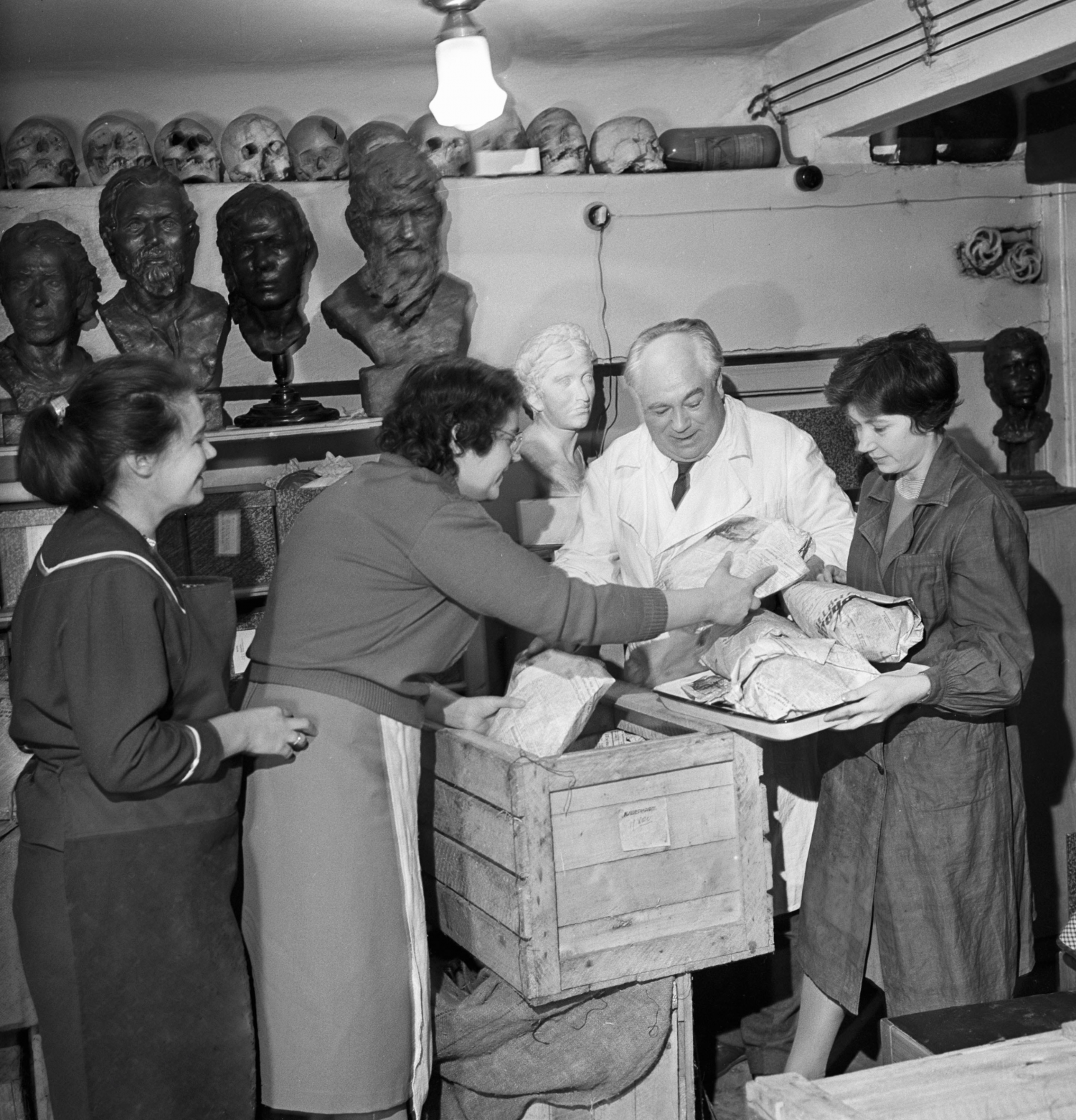 A man and three women in a laboratory surrounded by busts.