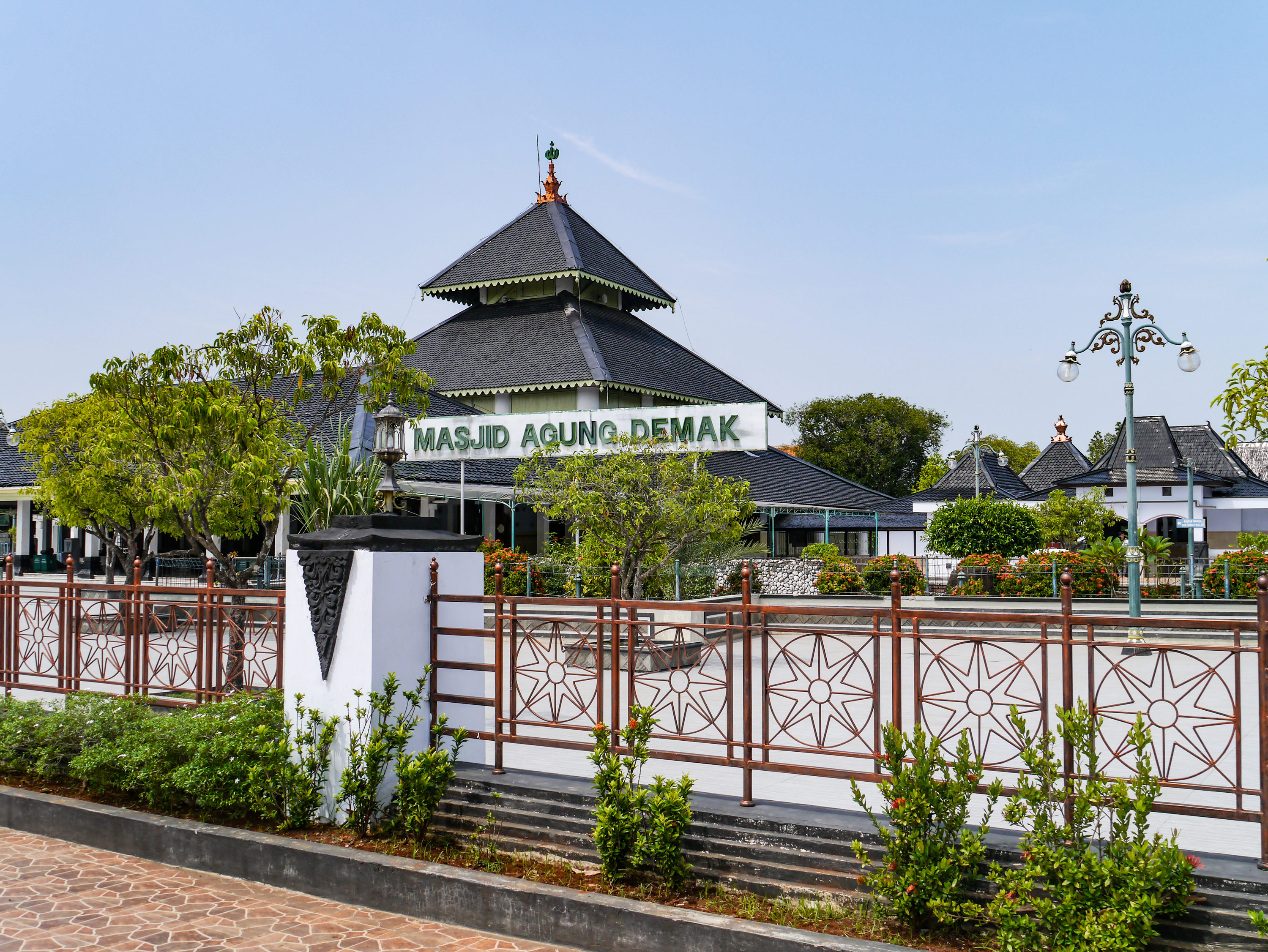 Mosque built as a three-tiered pagoda building with a large sign seen from behind a decorative fence.