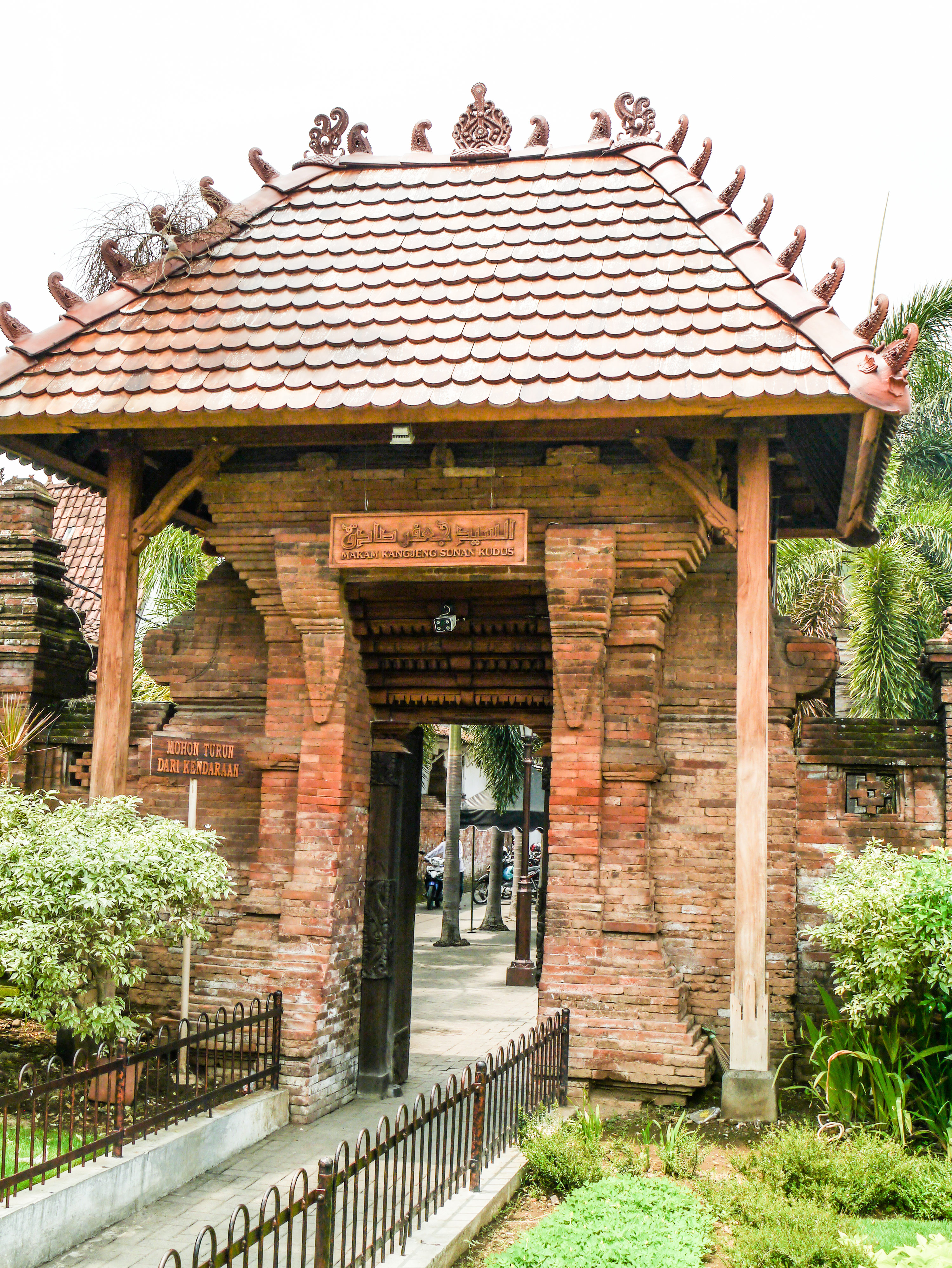 Gateway with a tiered pagoda-style roof supported by wooden beams atop a brick wall.
