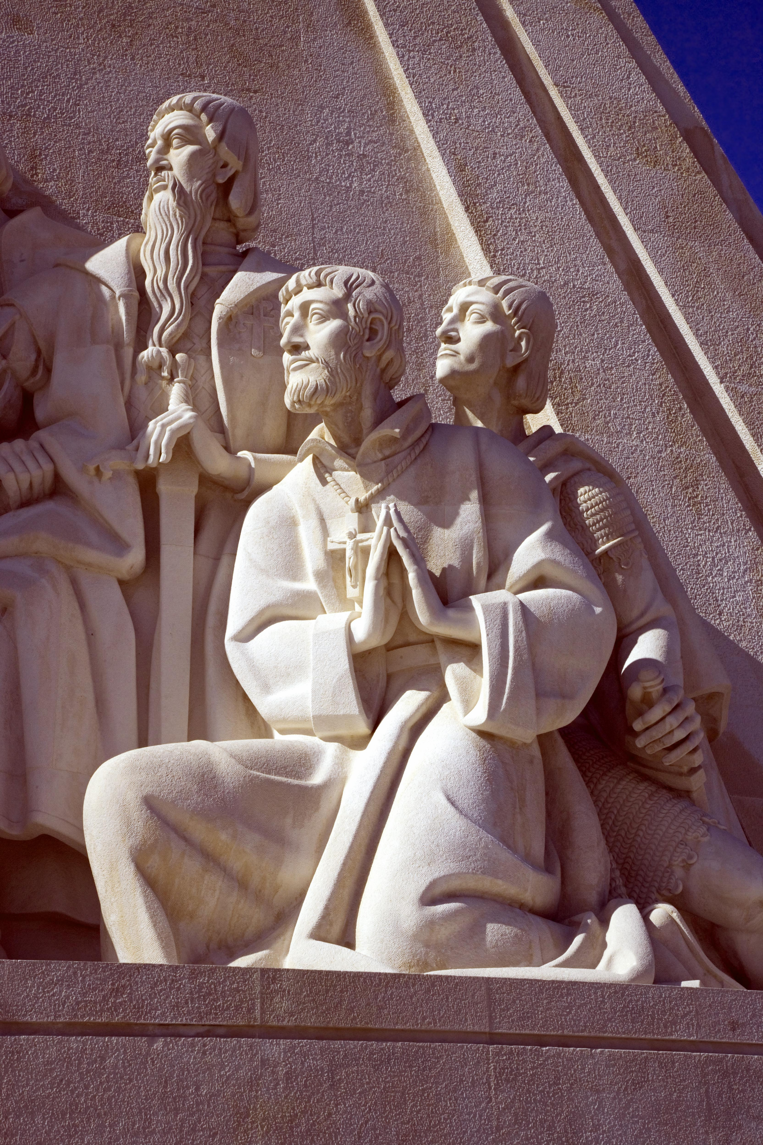 Detail from marble sculpture showing three figures facing left and looking up reverently. One of the figures has his hands joined in prayer.