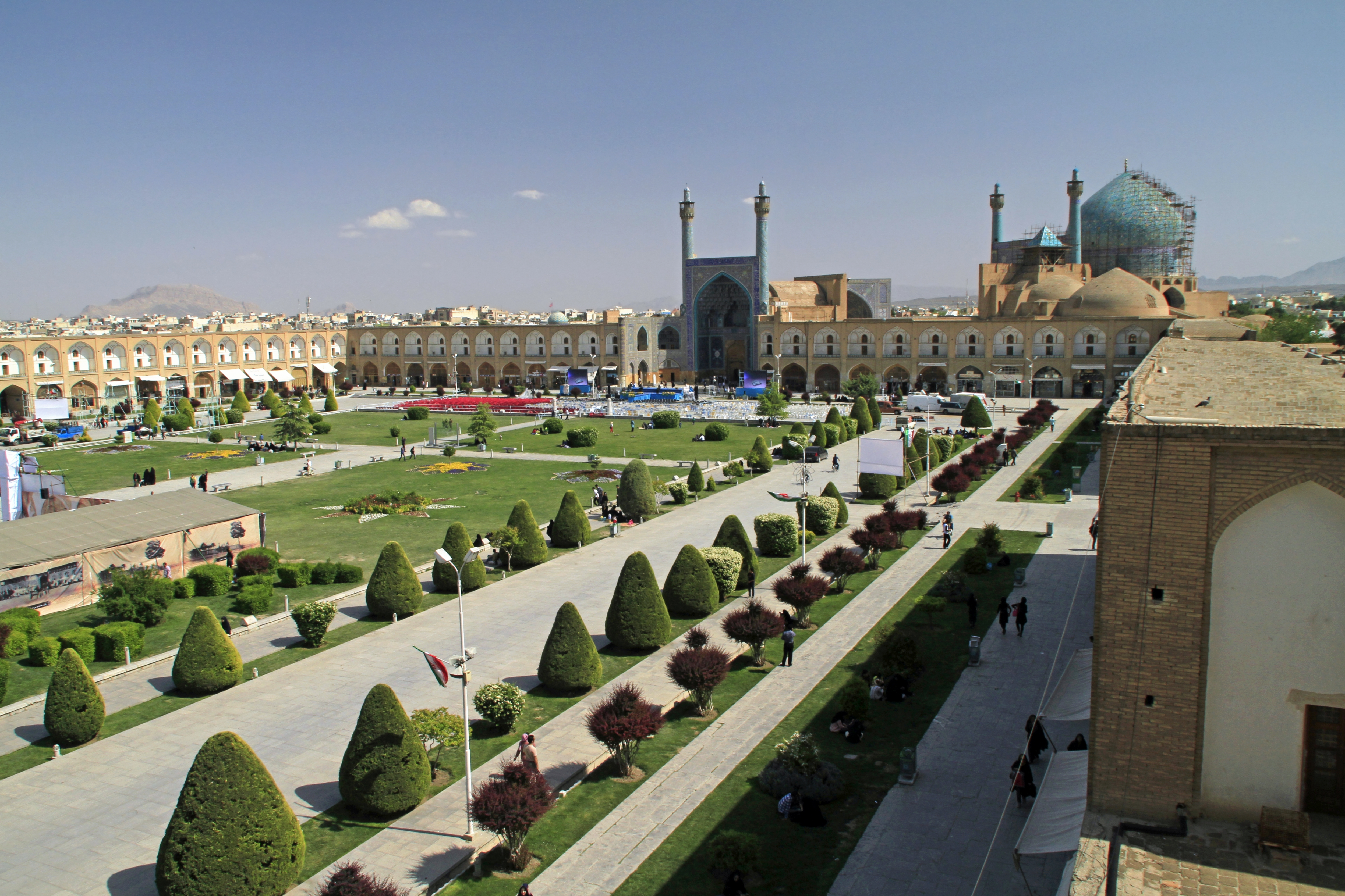 Panoramic view of a town square with a garden in the center flanked by buildings on three sides.