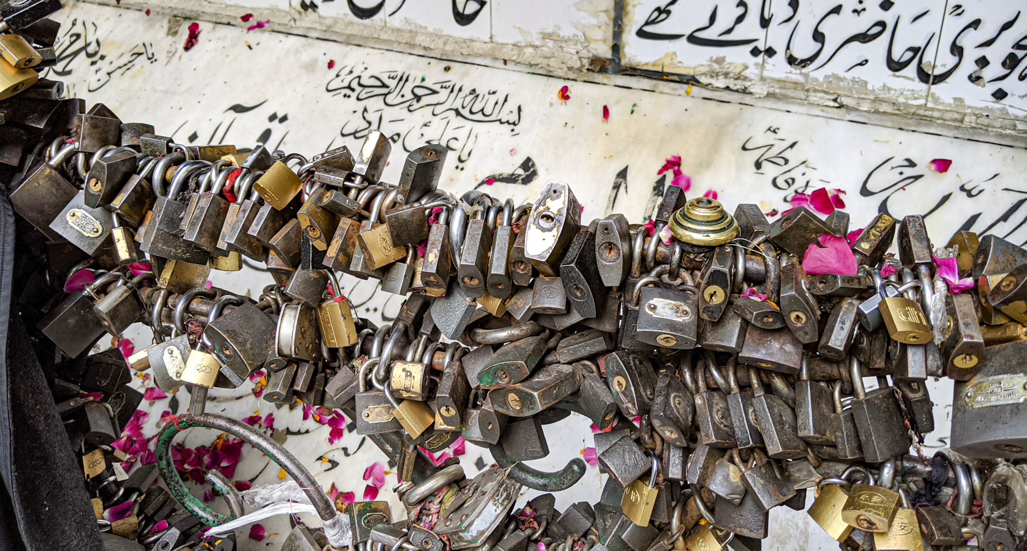 A large number of locks are placed along a wrought-iron surface. Arabic script is inscribed on some marble in the back.