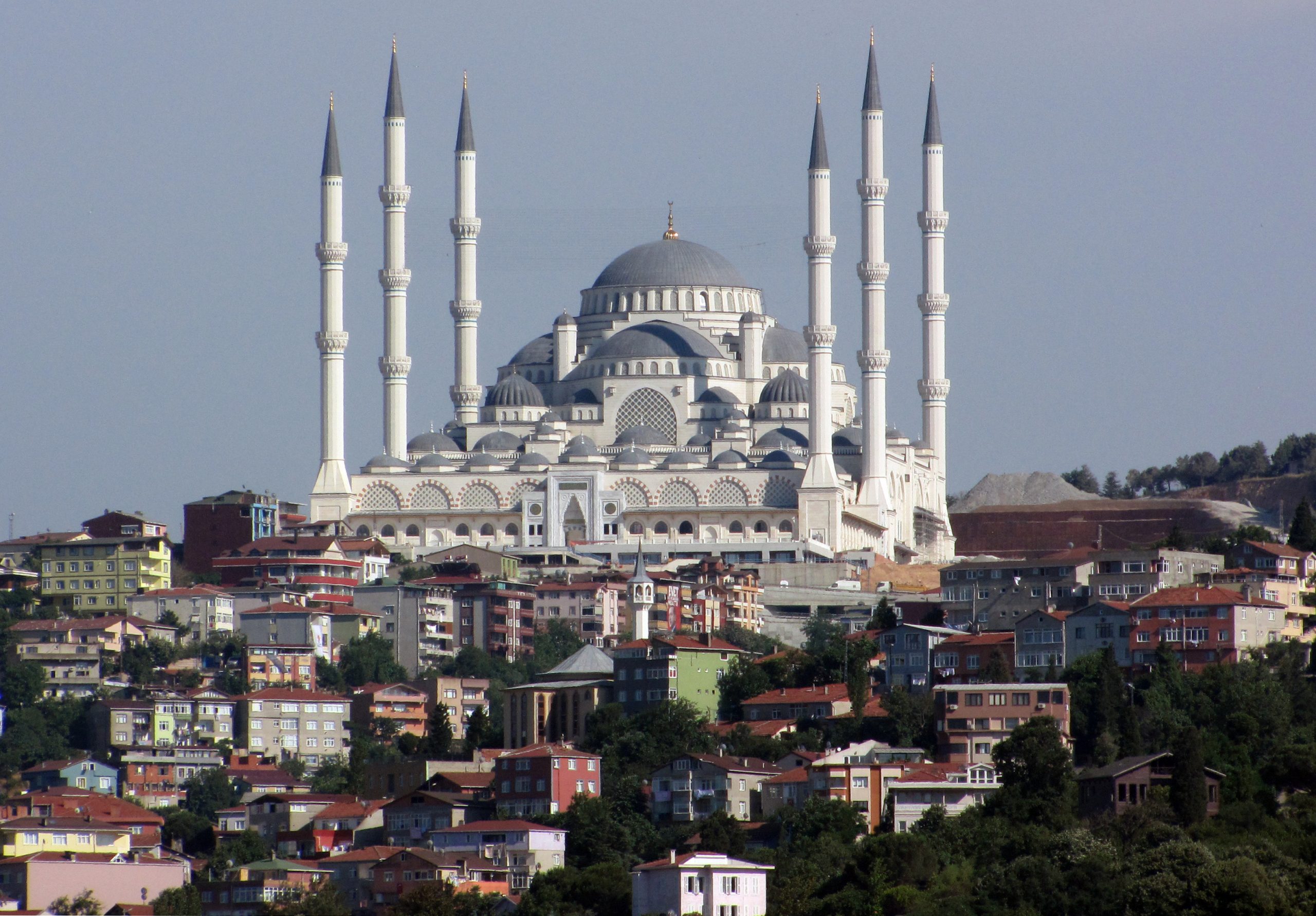White mosque with grey domes and six grey-topped minarets. The central dome and minarets have golden finials.