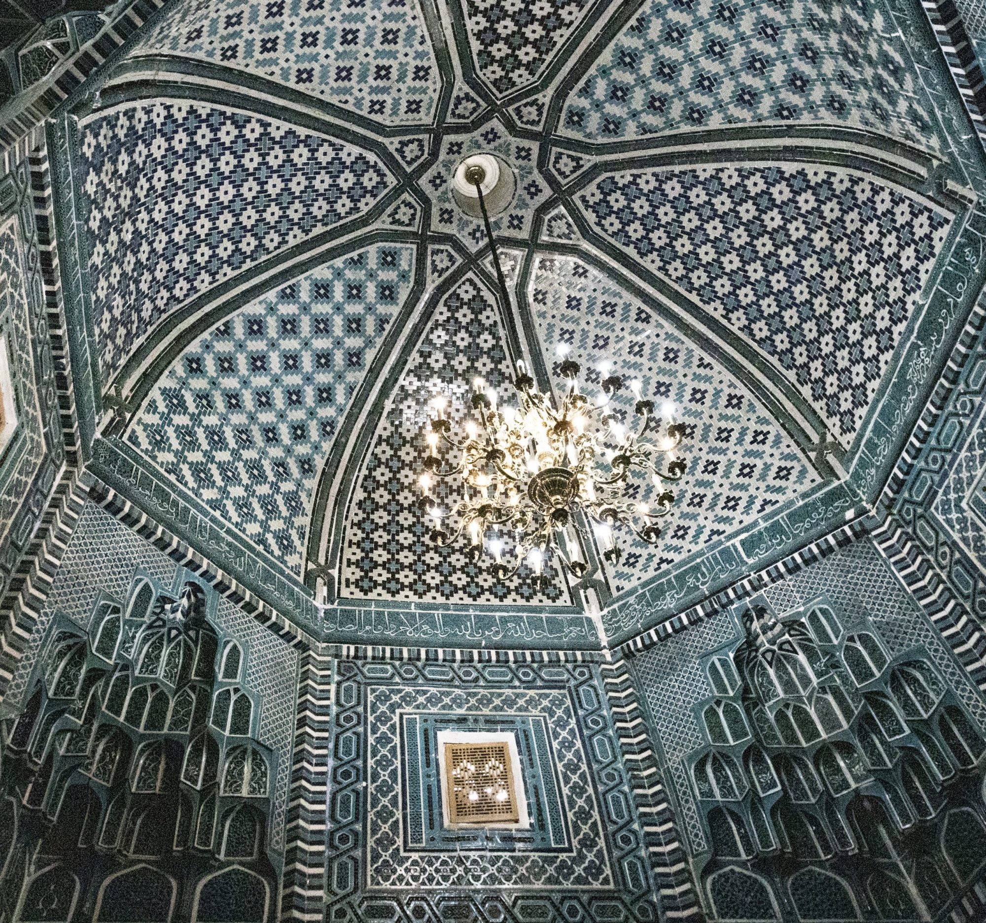 Decorated celing with shades of blue and white, a large hanging chandelier, and the honeycomb-esque (muqarnas) indentation in the walls.