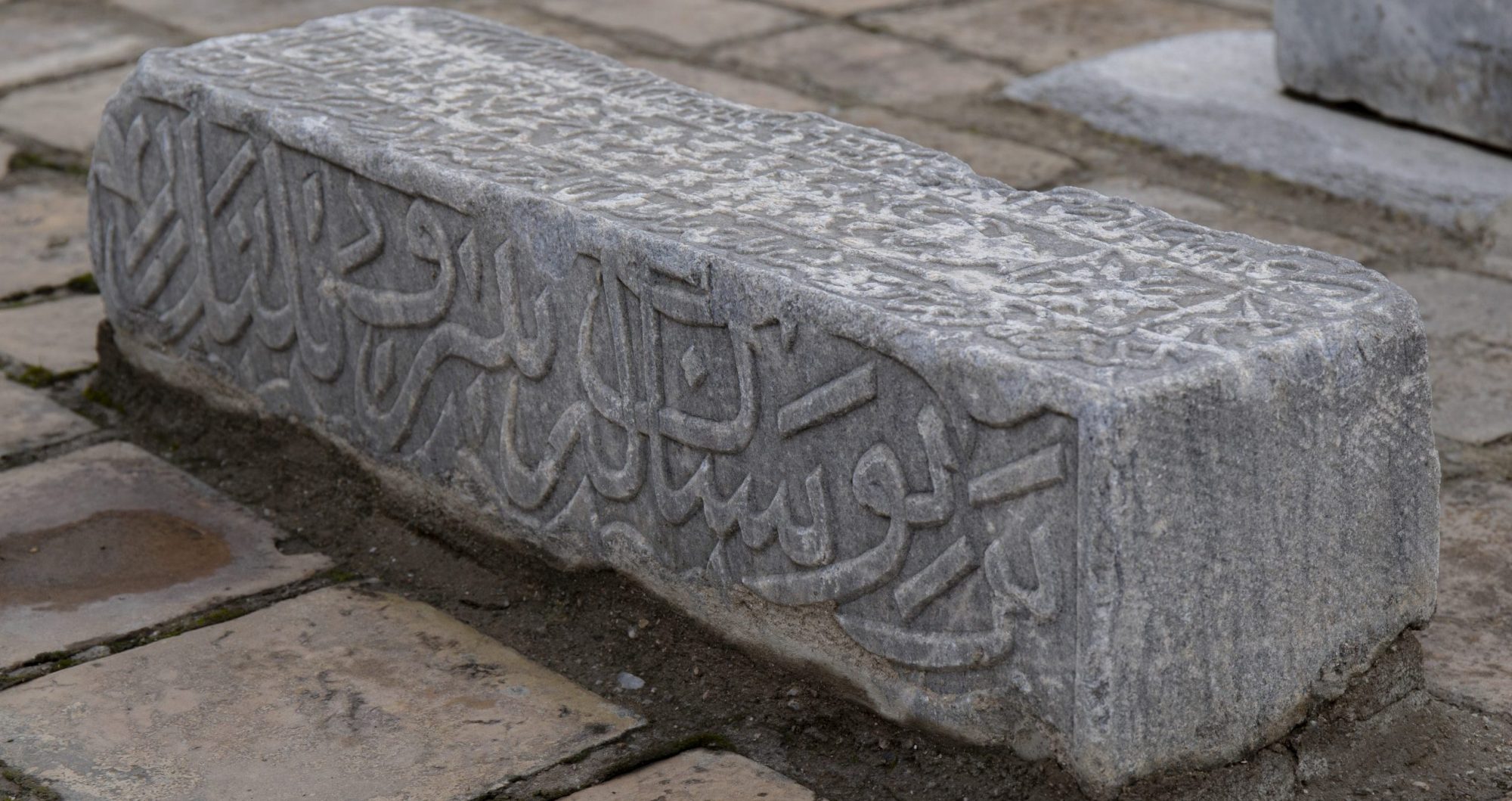 Detail of a gravestone with Arabic script calligraphy on its side.