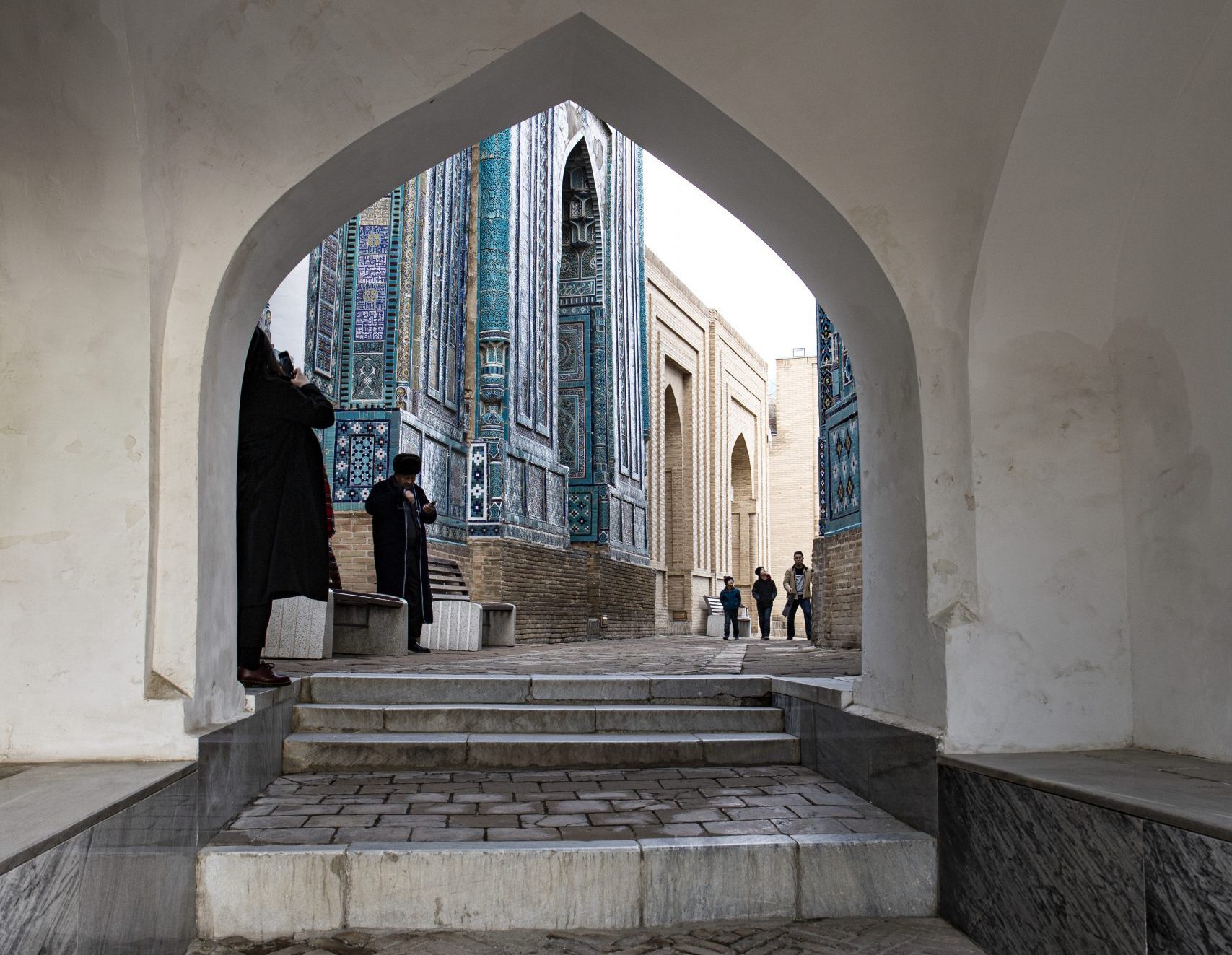 Passageway with stairs leading to a decorated building. Various visitors are seen observing the architecture.