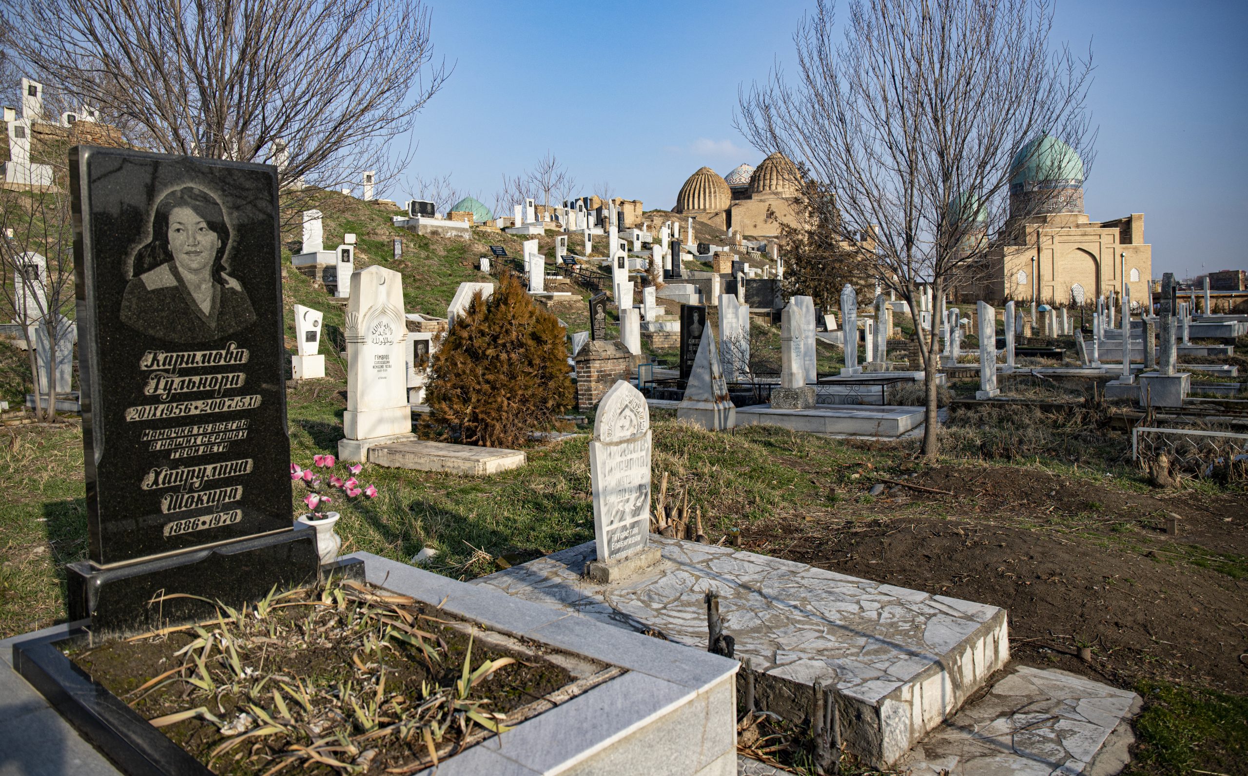 Graveyard with various tombstones. The most visible tombstone is black with the picture of a woman and Cyrillic script.